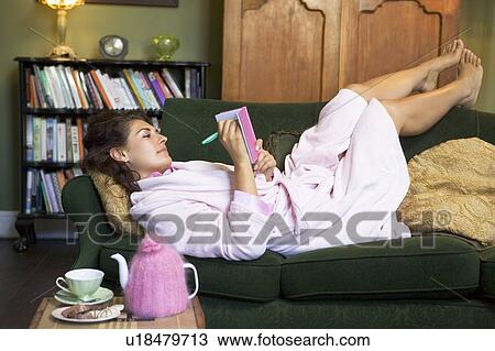 Young woman lying on sofa at home writing in her diary View Large Photo Image Stock Image - Young woman lying on sofa at home writing in her diary. Fotosearch