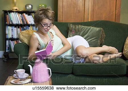 Stock Photo - Young woman lying on sofa at home writing in her diary. Fotosearch