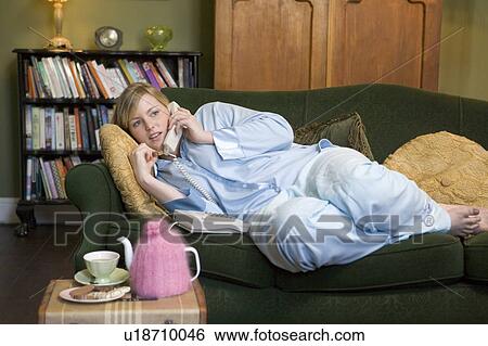 Stock Photograph - Young woman lying on sofa at home talking on telephone. Fotosearch
