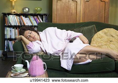 Stock Image - Young woman lying on sofa falling asleep while watching television. Fotosearch