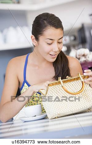 Young woman sitting at a table checking her handbag View Large Photo Image Stock Image - Young woman sitting at a table checking her handbag. Fotosearch