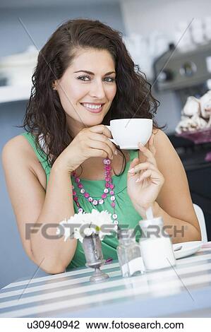 Stock Image - Young woman sitting at a table drinking tea. Fotosearch