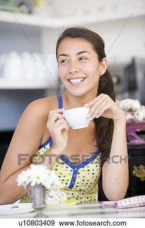 Young woman sitting at a table drinking tea View Large Photo Image Stock Photo - Young woman sitting at a table drinking tea. Fotosearch