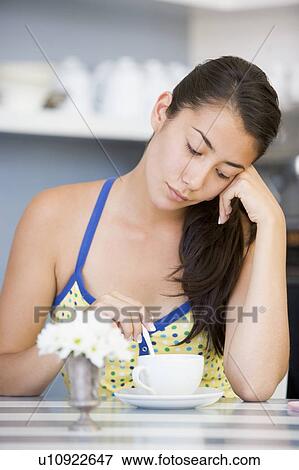 Stock Photo - Young woman sitting at a table drinking tea. Fotosearch