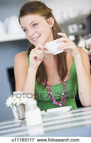 Stock Photo - Young woman sitting at a table drinking tea. Fotosearch