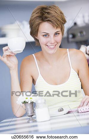 Young woman sitting at a table drinking tea View Large Photo Image Stock Photograph - Young woman sitting at a table drinking tea. Fotosearch