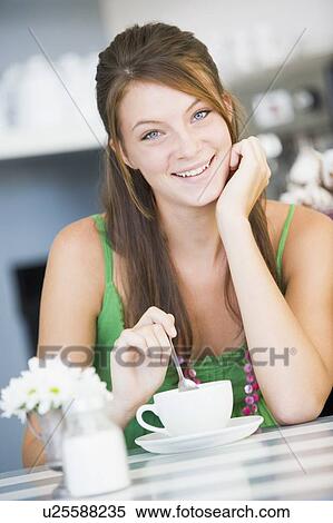 Young woman sitting at a table drinking tea View Large Photo Image Stock Photography - Young woman sitting at a table drinking tea. Fotosearch