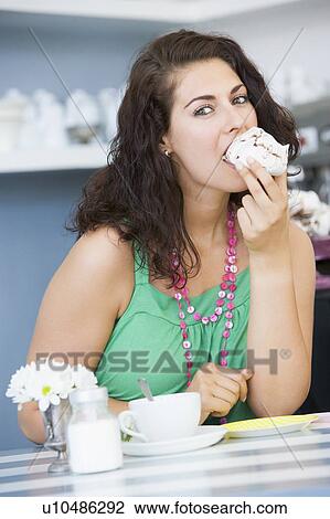 Stock Image - Young woman sitting at a table eating a sweet treat. Fotosearch