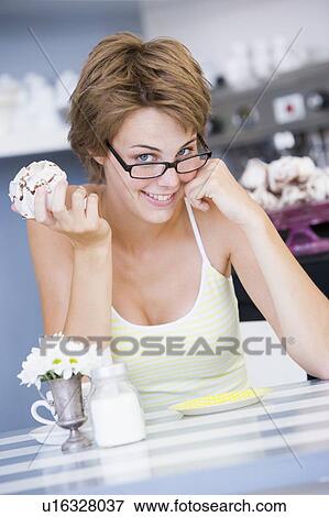 Young woman sitting at a table eating a sweet treat View Large Photo Image Stock Photo - Young woman sitting at a table eating a sweet treat. Fotosearch