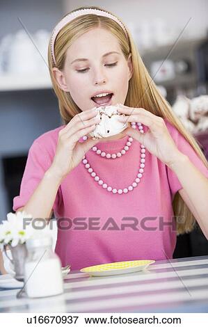 Stock Photo - Young woman sitting at a table eating a sweet treat. Fotosearch