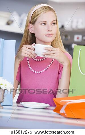 Young woman sitting at a table taking a break from shopping and drinking tea View Large Photo Image Stock Photography - Young woman sitting at a table taking a break from shopping and drinking tea. Fotosearch
