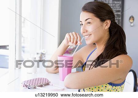 Young woman sitting by a window and having a cold drink View Large Photo Image Stock Image - Young woman sitting by a window and having a cold drink. Fotosearch