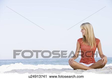 Stock Image - Young woman sitting on a beach. Fotosearch