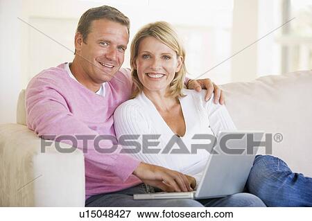 Stock Photo - Couple in living room using laptop and smiling. Fotosearch