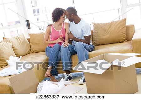 Stock Photo - Couple relaxing with champagne by boxes in new home smiling. Fotosearch