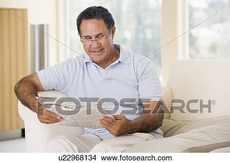 Picture - Man in living room reading newspaper smiling. Fotosearch