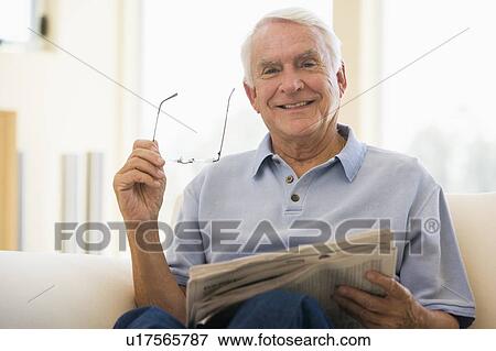 Man in living room reading newspaper smiling View Large Photo Image Stock Photo - Man in living room reading newspaper smiling. Fotosearch