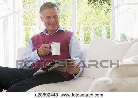 Man in living room with coffee reading newspaper smiling View Large Photo Image Stock Photo - Man in living room with coffee reading newspaper smiling. Fotosearch