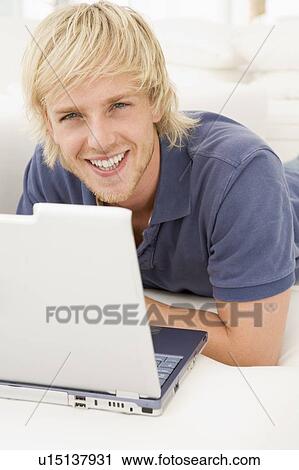 Stock Image - Man in living room with laptop smiling. Fotosearch