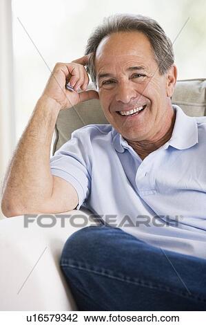 Man sitting in living room smiling View Large Photo Image Stock Image - Man sitting in living room smiling. Fotosearch