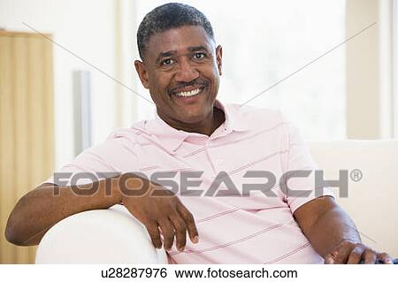 Stock Photograph - Man sitting in living room smiling. Fotosearch