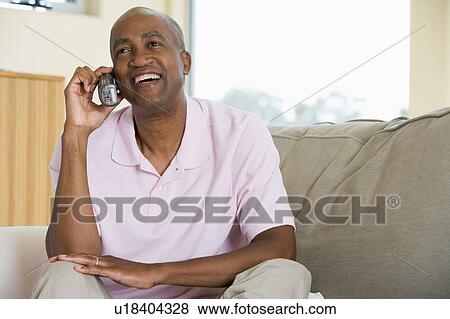 Man sitting in living room using telephone and smiling View Large Photo Image Stock Photo - Man sitting in living room using telephone and smiling. Fotosearch