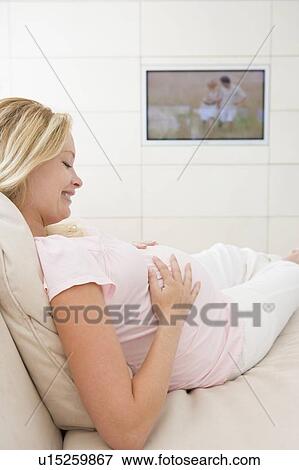 Stock Photo - Pregnant woman watching television smiling. Fotosearch
