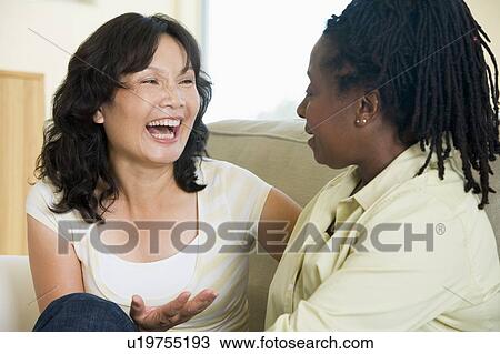 Stock Image - Two women talking in living room and smiling. Fotosearch