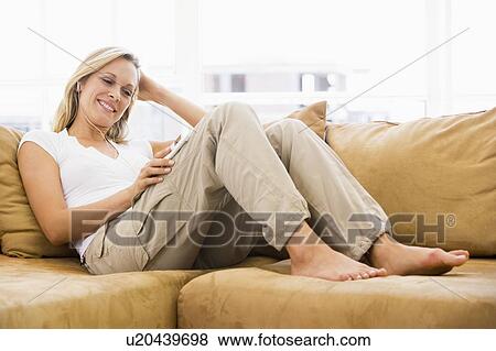 Stock Photo - Woman in living room listening to MP3 player smiling. Fotosearch