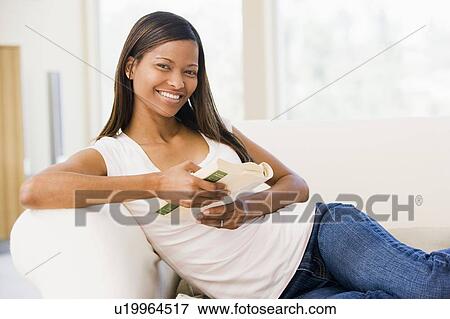 Stock Photo - Woman in living room reading book smiling. Fotosearch