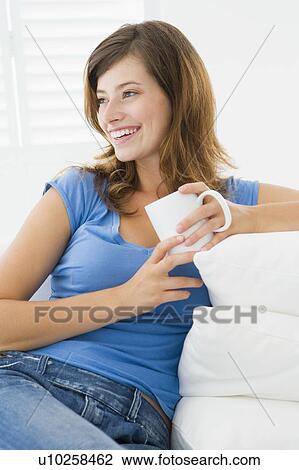 Stock Image - Woman in living room with coffee smiling. Fotosearch