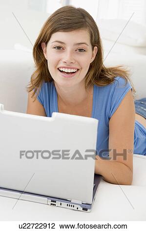 Stock Image - Woman in living room with laptop smiling. Fotosearch