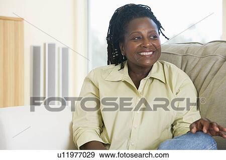 Stock Photo - Woman sitting in living room smiling. Fotosearch