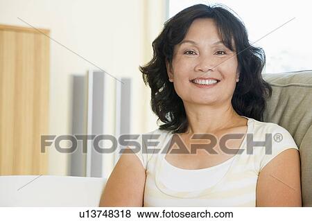 Stock Photo - Woman sitting in living room smiling. Fotosearch