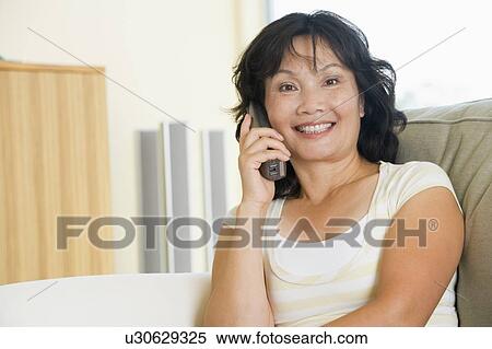 Woman sitting in living room using telephone and smiling View Large Photo Image Stock Photography - Woman sitting in living room using telephone and smiling. Fotosearch