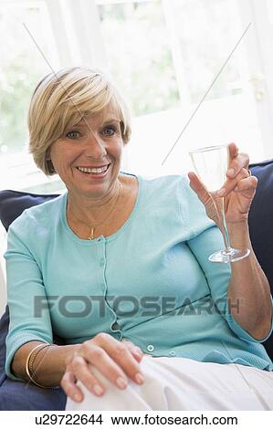 Woman sitting in living room with drink smiling View Large Photo Image Picture - Woman sitting in living room with drink smiling. Fotosearch