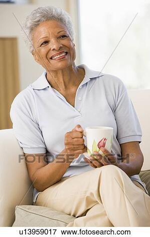 Stock Photo - Woman sitting in living room with coffee smiling. Fotosearch