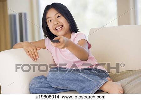 Picture - Young girl in living room with remote control smiling. Fotosearch