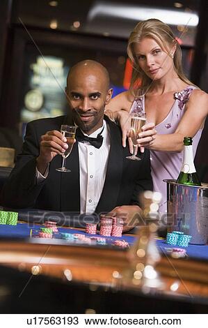Couple in casino at roulette table holding champagne and smiling (selective focus) View Large Photo Image Stock Image - Couple in casino at roulette table holding champagne and smiling (selective focus). Fotosearch