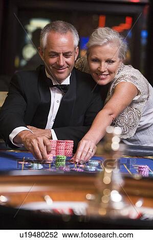 Stock Image - Couple in casino playing roulette and smiling (selective focus). Fotosearch