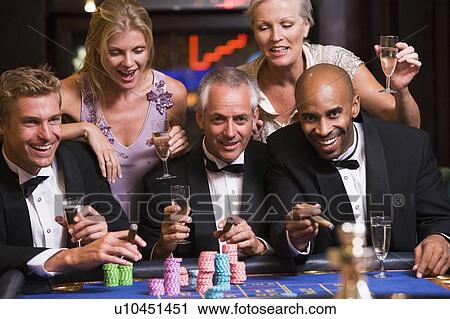 Stock Image - Five people in casino playing roulette and smiling (selective focus). Fotosearch