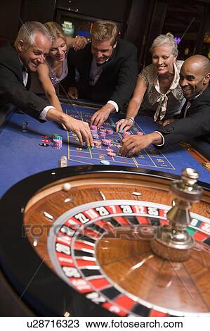 Stock Image - Group of people in casino playing roulette and smiling (selective focus). Fotosearch
