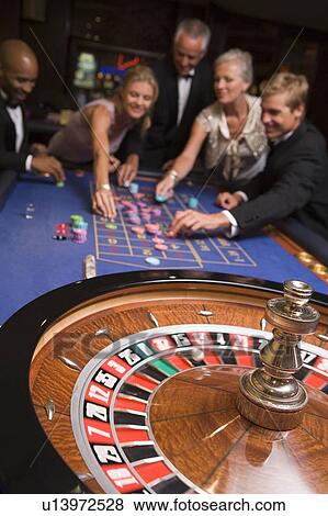 Stock Photo - Group of people in casino playing roulette and smiling (selective focus). Fotosearch
