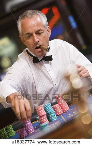 Man in casino playing roulette and smoking cigar (selective focus) View Large Photo Image Picture - Man in casino playing roulette and smoking cigar (selective focus). Fotosearch
