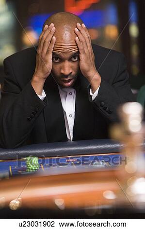 Stock Image - Man in casino playing roulette and losing (selective focus). Fotosearch
