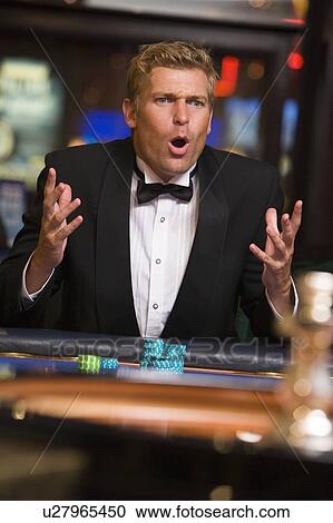 Stock Image - Man in casino playing roulette and losing (selective focus). Fotosearch