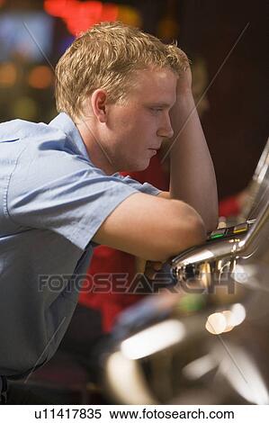 Man in casino playing slot machine frustrated with people in background (selective focus) View Large Photo Image Stock Photography - Man in casino playing slot machine frustrated with people in background (selective focus). Fotosearch
