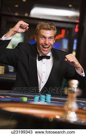 Stock Image - Man in casino winning at roulette and smiling (selective focus). Fotosearch