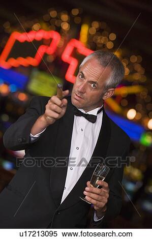 Stock Photography - Man in casino with cigar and champagne pointing (selective focus). Fotosearch
