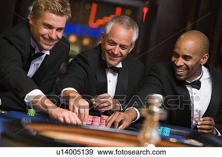 Stock Photo - Three men in casino playing roulette smiling (selective focus). Fotosearch